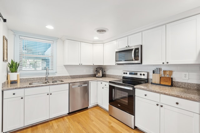 kitchen with stainless steel appliances, visible vents, light wood-style floors, white cabinets, and a sink