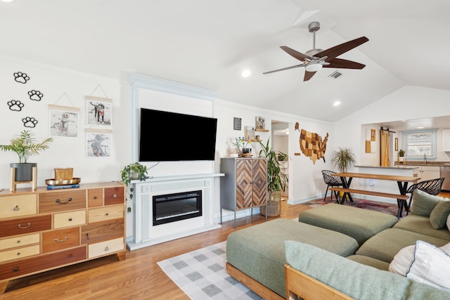 living area featuring visible vents, a glass covered fireplace, ceiling fan, vaulted ceiling, and light wood-type flooring