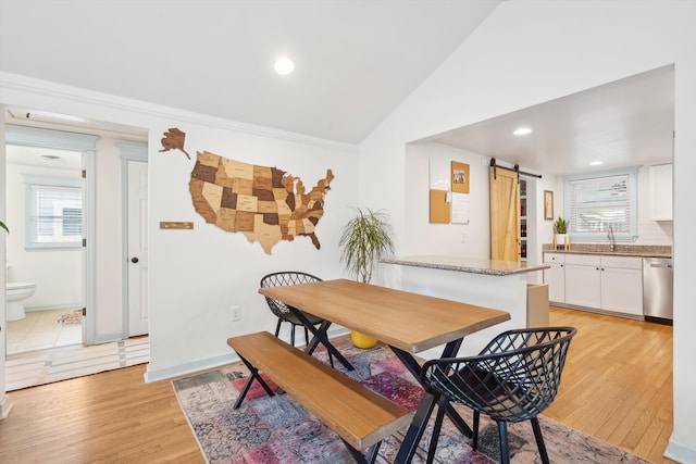 dining area featuring plenty of natural light, vaulted ceiling, light wood-style flooring, and a barn door