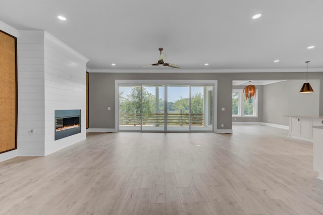 unfurnished living room featuring ceiling fan, a large fireplace, a healthy amount of sunlight, and ornamental molding