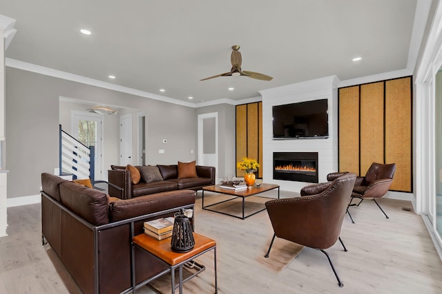 living room with ceiling fan, a large fireplace, light hardwood / wood-style floors, and ornamental molding