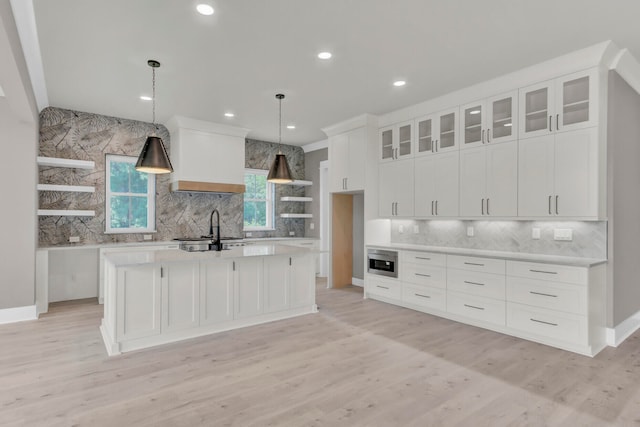 kitchen with sink, tasteful backsplash, pendant lighting, a kitchen island with sink, and white cabinets