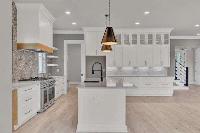 kitchen with white cabinetry, sink, an island with sink, decorative light fixtures, and range with two ovens