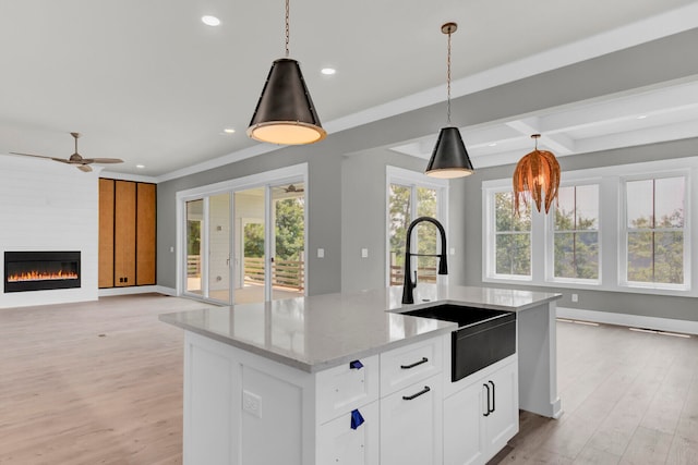 kitchen with light stone countertops, sink, pendant lighting, white cabinets, and an island with sink