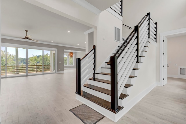 stairway with ceiling fan, hardwood / wood-style floors, and ornamental molding