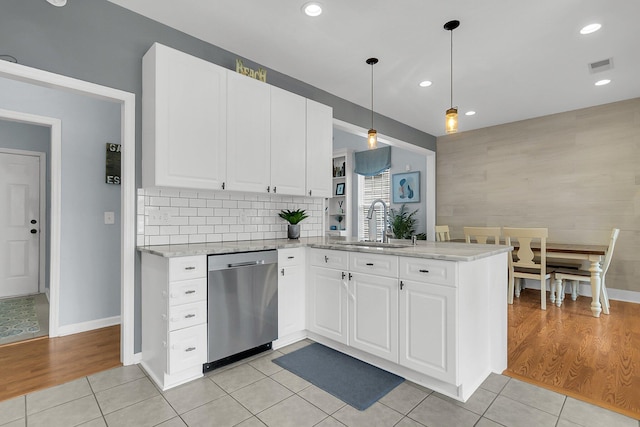 kitchen featuring visible vents, a sink, a peninsula, light tile patterned floors, and dishwasher