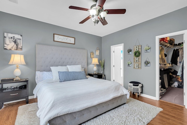 bedroom with a walk in closet, baseboards, wood finished floors, a closet, and a ceiling fan