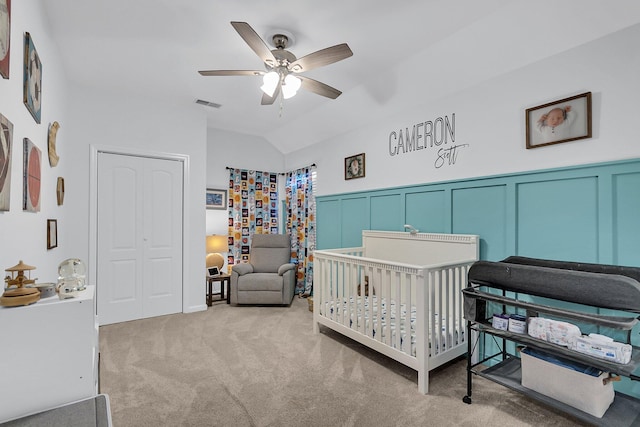 bedroom featuring carpet, visible vents, a crib, vaulted ceiling, and a decorative wall