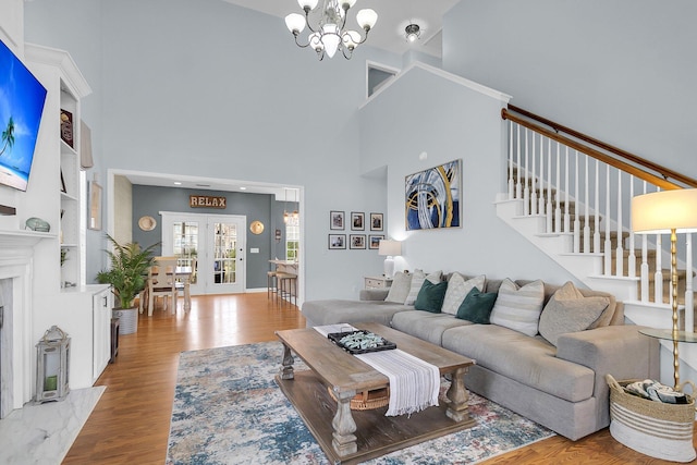 living room with stairway, a towering ceiling, an inviting chandelier, and wood finished floors