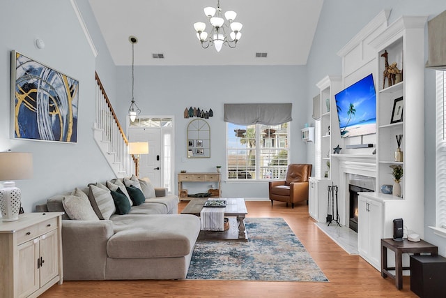 living area with visible vents, a fireplace with flush hearth, stairway, light wood-style floors, and a notable chandelier