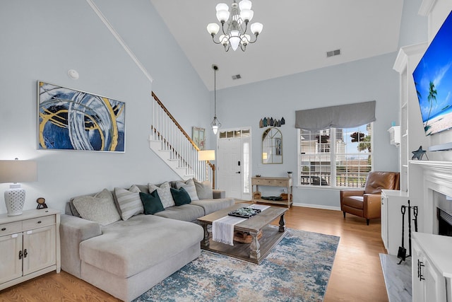 living area with high vaulted ceiling, light wood-style flooring, a fireplace, stairs, and a chandelier