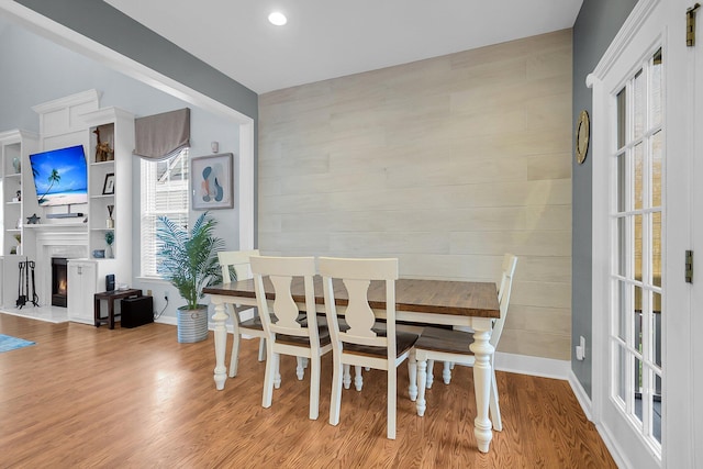 dining room featuring a wealth of natural light, a warm lit fireplace, and wood finished floors