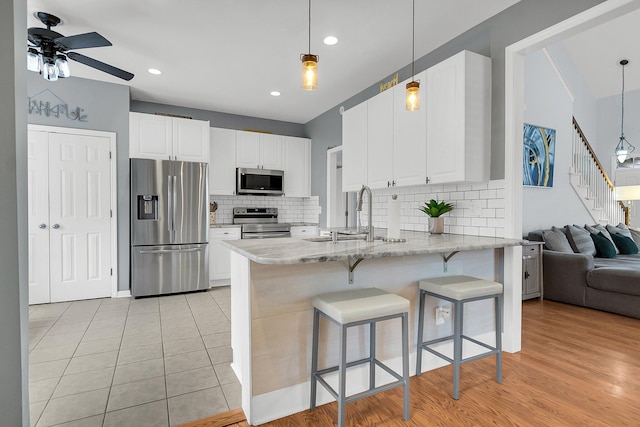 kitchen featuring a breakfast bar area, light stone countertops, a peninsula, a sink, and appliances with stainless steel finishes