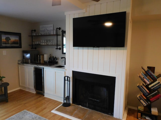 bar with sink, wine cooler, a fireplace, light hardwood / wood-style flooring, and white cabinets