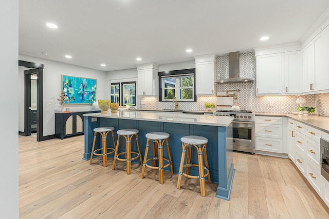 kitchen featuring a center island, wall chimney range hood, high end stainless steel range, white cabinets, and a kitchen breakfast bar