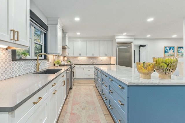 kitchen featuring white cabinets, high quality appliances, light stone counters, a spacious island, and sink