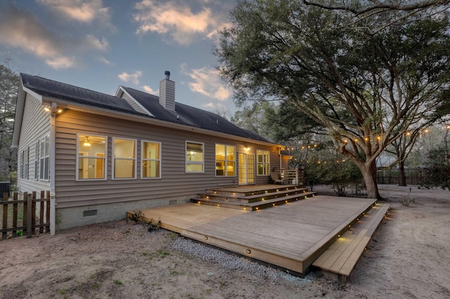 back of property at dusk with crawl space, a chimney, a deck, and fence