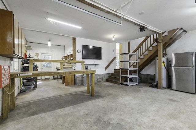 basement featuring a workshop area, stairs, freestanding refrigerator, and a garage