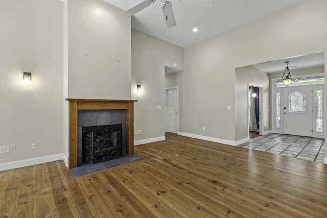 unfurnished living room featuring a tiled fireplace, baseboards, and wood-type flooring