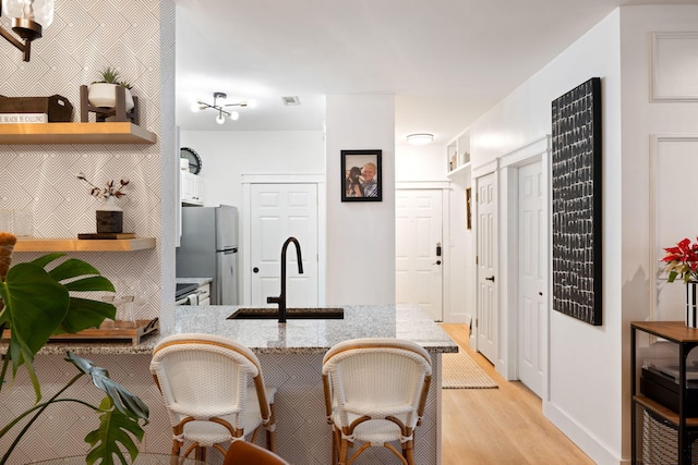 kitchen with sink, light hardwood / wood-style floors, light stone counters, kitchen peninsula, and stainless steel refrigerator