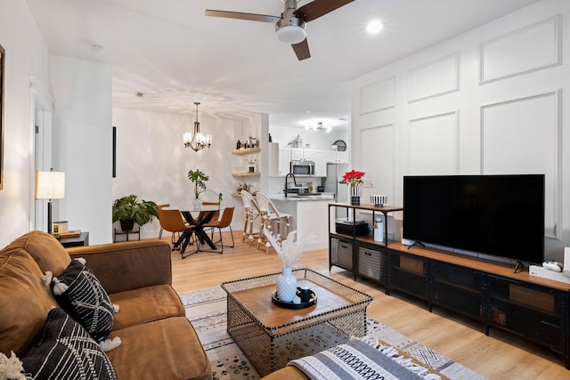 living room with sink, light hardwood / wood-style floors, and ceiling fan with notable chandelier