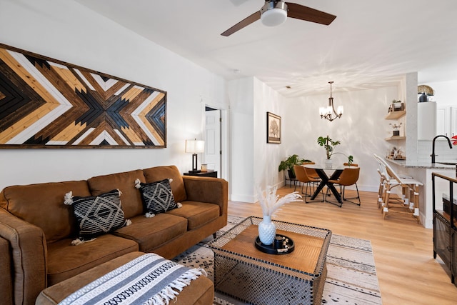 living room featuring ceiling fan with notable chandelier, light wood-type flooring, and sink