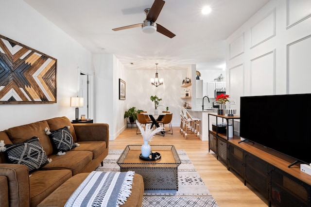 living room featuring ceiling fan with notable chandelier, light hardwood / wood-style floors, and sink