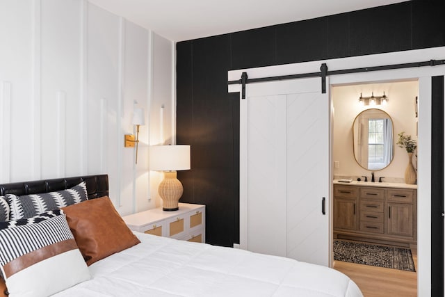 bedroom with a barn door, ensuite bathroom, and light wood-type flooring