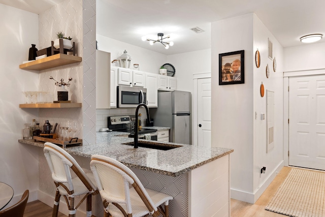 kitchen featuring a kitchen breakfast bar, light hardwood / wood-style flooring, light stone counters, kitchen peninsula, and stainless steel appliances