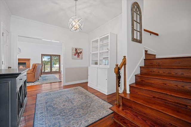 entryway featuring a warm lit fireplace, baseboards, dark wood-style flooring, stairs, and crown molding