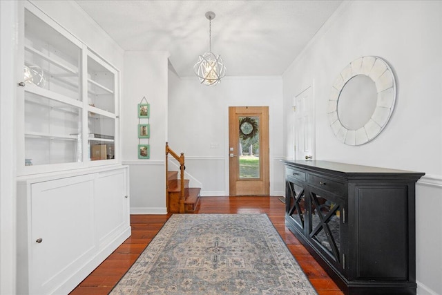 foyer entrance with dark wood-style flooring, an inviting chandelier, ornamental molding, baseboards, and stairs