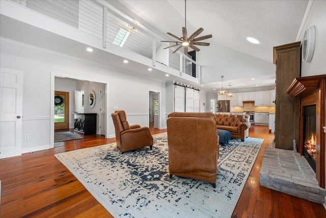 living area featuring a warm lit fireplace, baseboards, high vaulted ceiling, and hardwood / wood-style flooring