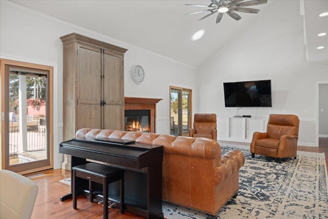 living area with crown molding, light wood finished floors, a ceiling fan, a glass covered fireplace, and high vaulted ceiling