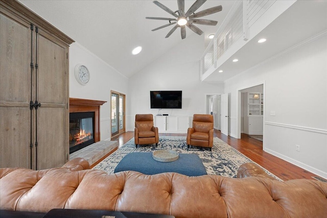 living area featuring ceiling fan, high vaulted ceiling, wood finished floors, a glass covered fireplace, and crown molding