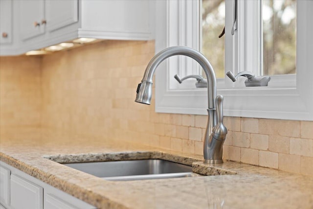 room details featuring light stone countertops, a sink, white cabinetry, and decorative backsplash