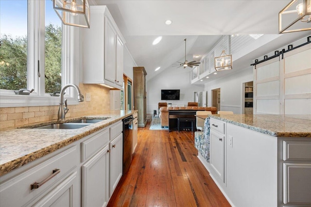 kitchen featuring a barn door, dishwasher, vaulted ceiling, white cabinetry, and a sink