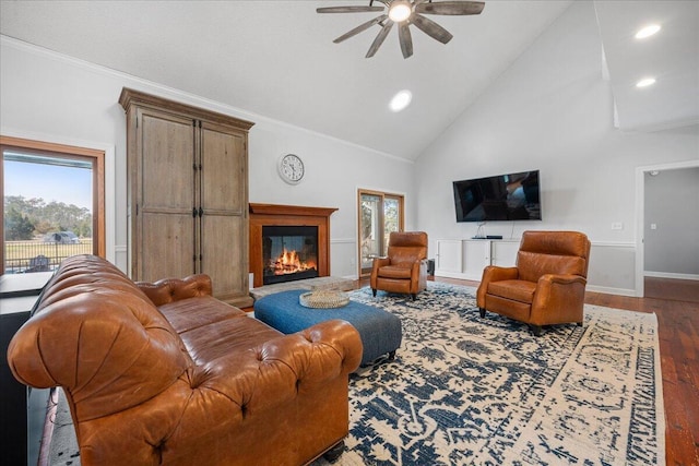 living room featuring ceiling fan, high vaulted ceiling, wood finished floors, ornamental molding, and a glass covered fireplace