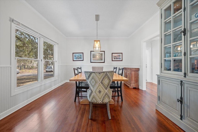 dining area featuring a wainscoted wall, a textured ceiling, ornamental molding, and dark wood-style flooring