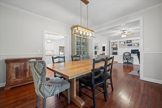 dining space featuring dark wood finished floors, a ceiling fan, wainscoting, crown molding, and built in shelves