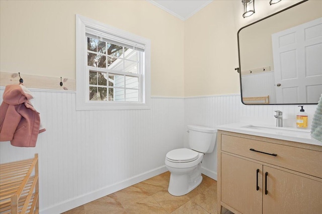 half bathroom with a wainscoted wall, ornamental molding, vanity, and toilet