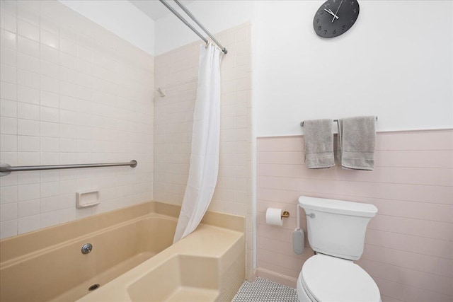 bathroom featuring toilet, a wainscoted wall, tile walls, and shower / tub combo with curtain