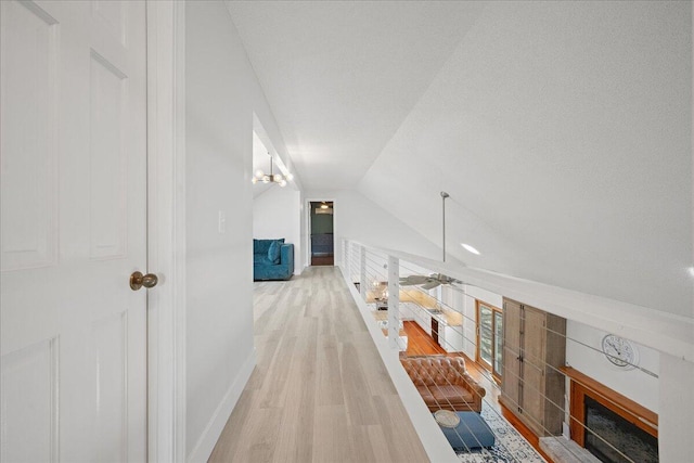 hall with light wood-style floors, baseboards, and vaulted ceiling