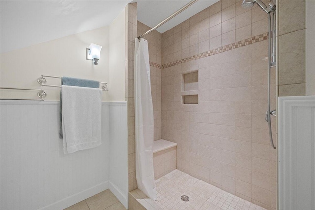 full bath featuring lofted ceiling, wainscoting, a shower stall, and tile patterned flooring