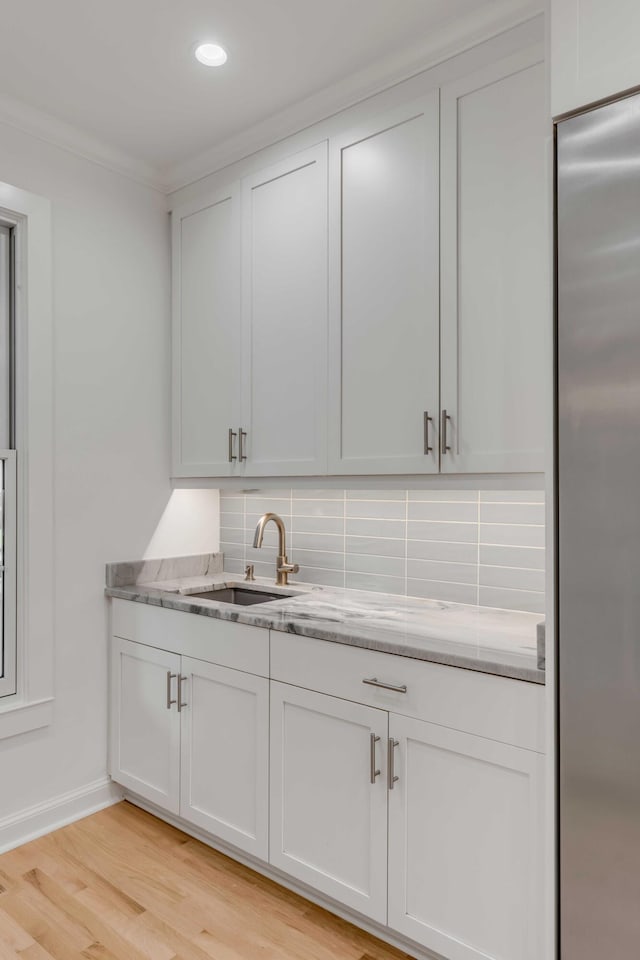 bar with backsplash, white cabinets, light wood-type flooring, and stainless steel refrigerator