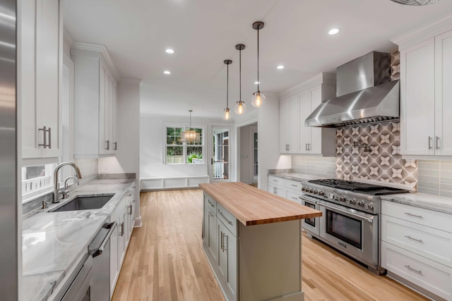 kitchen with butcher block countertops, a center island, white cabinetry, stainless steel appliances, and wall chimney exhaust hood