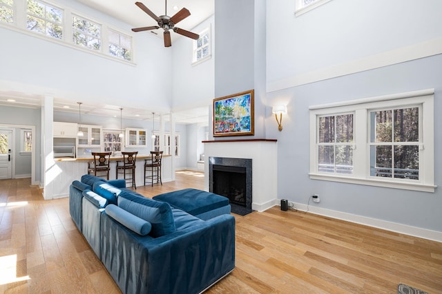 living room with light wood finished floors, a fireplace with flush hearth, baseboards, and a ceiling fan