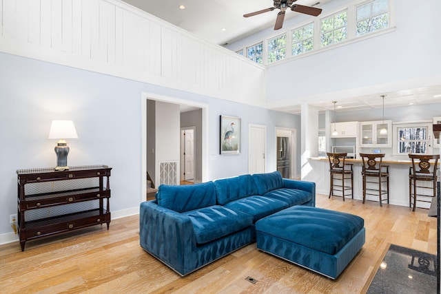 living room with baseboards, ceiling fan, recessed lighting, light wood-style flooring, and a high ceiling