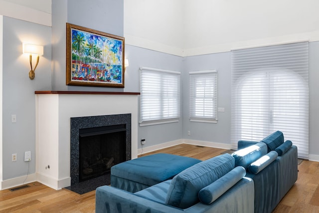 living area featuring a fireplace with flush hearth, wood finished floors, visible vents, and baseboards