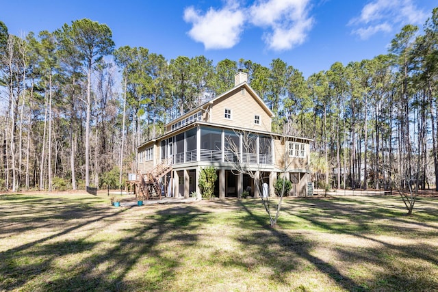 rear view of house with stairway, a yard, a chimney, and a sunroom