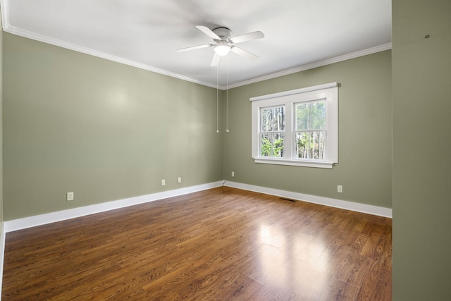 empty room with a ceiling fan, visible vents, wood finished floors, baseboards, and ornamental molding